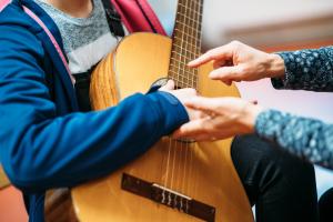 Ein Lehrer der Musik- und Kunstschule unterrichtet das Spielen einer Gitarre