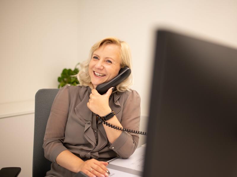 Eine Frau sitzt an einem Schreibtisch mit Monitor und telefoniert