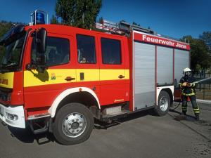 Ein Feuerwehrmann steht vor einem Einsatzfahrzeug und hat einen Schlauch zum Löschen eines Brandes in der Hand