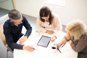 Ein Mann und 2 Frauen in einem Gespräch an einem Tisch, Bild ist von oben aufgenommen