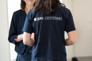 Frau steht mit dem Rücken zur Kamera, auf ihrem T-Shirt steht der Schriftzug "Jena. Lichtstadt"