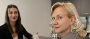 Zwei Personen sitzen am Tisch und schauen in die Kamera.