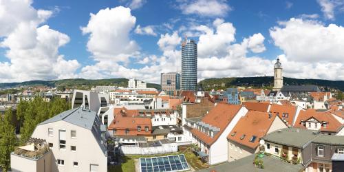 Panoramablick über Jena mit Jentower, vielen Häusern, einigen Bäumen und den Bergen im Hintergrund