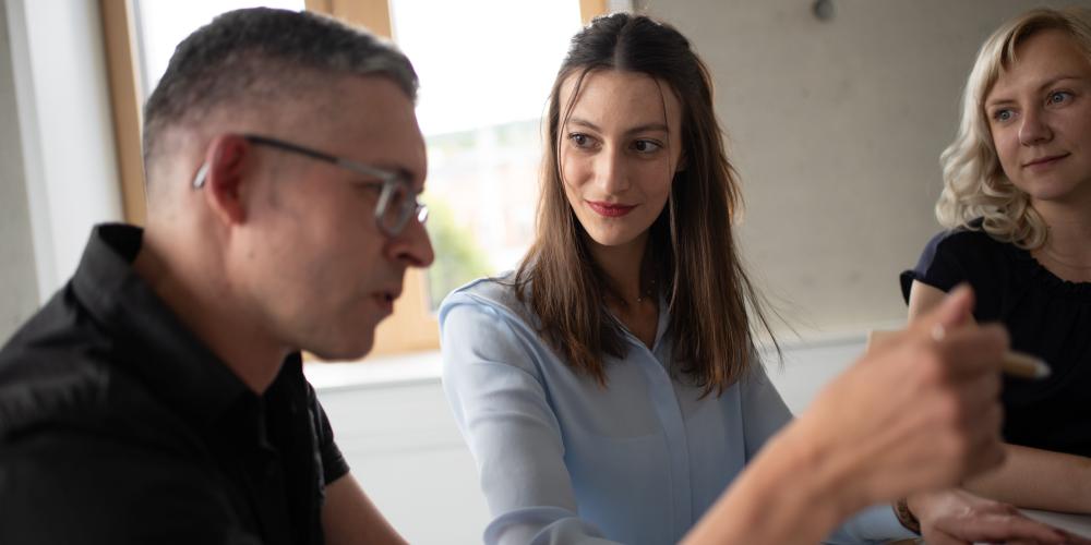 Ein Mann und zwei Frauen in einem Raum am Tisch