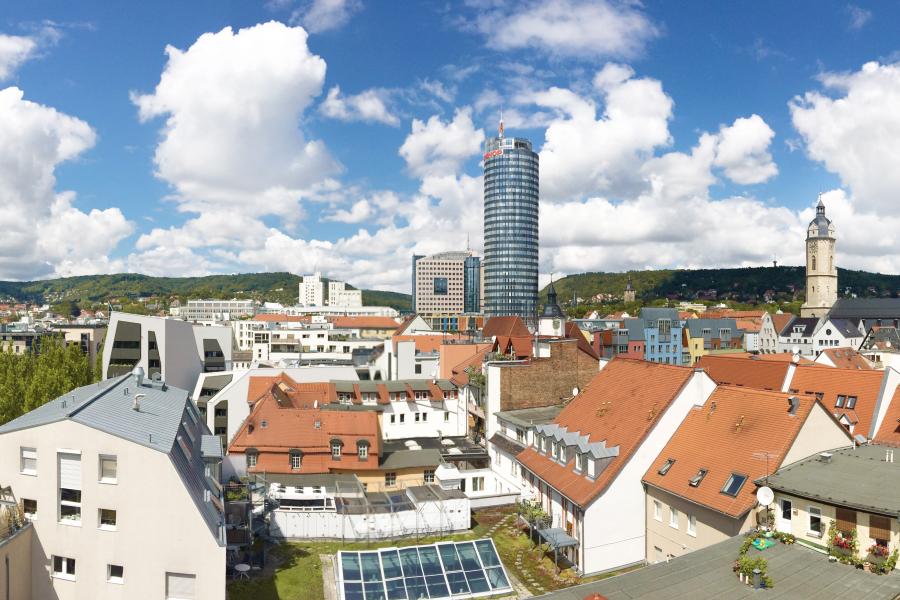 Blick auf Jena. Im Hintergrund der blaue Himmel mit weißen Wolken. Im Vordergrund Häuser der Jenaer Innenstadt.